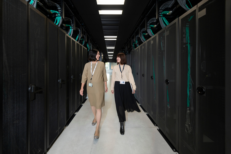 Two women with work badges smiling in a computer server room